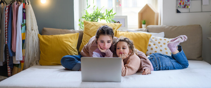 Sisters indoors at home, using laptop. Lockdown concept.