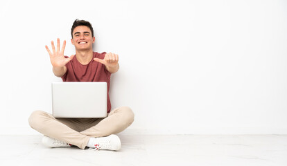 Teenager man sitting on the flor with his laptop counting six with fingers