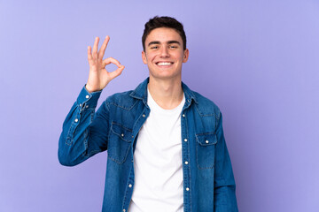 Teenager caucasian  handsome man isolated on purple background showing ok sign with fingers