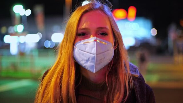 [4k] young woman putting on ffp2 mask in colorful streetlight