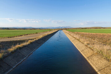 Water channel for irrigation in landscape with mountains in the background and path parallel to the canal 