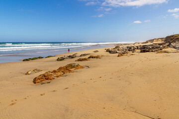 Sunny beach with sand and rocks in the sand and a single person strolling. Razo beach. Arnados. Galicia, Spain