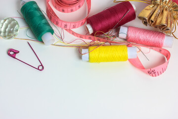 Reels of multicolored thread, pink measuring tape, and a pink pin on a white table flatlay. Needlework, sewing, and repair of the clothes. Space for text.