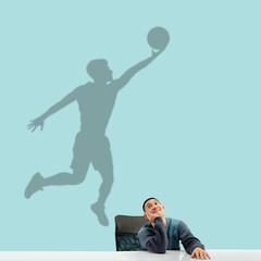 Fototapeta na wymiar Young asian man dreaming about future in big sport during his work in office. Becoming a legend. Shadow, silhouette of professional basketball player on the wall. Inspiration, aspiration. Copyspace.