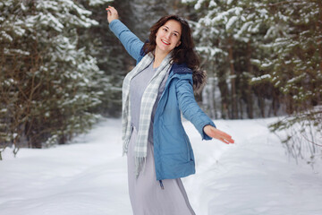 Conception of winter holidays. Cheerful girl in warm clothes playing with snow outdoors near forest