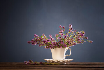 thyme flowers in white vintage cup on wooden table on blue background
