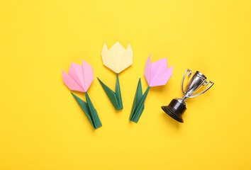 Origami tulips and winner cup on yellow background. Victory concept. Flat lay. Top view