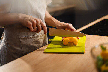 Caucasian woman wearing apron cutting bell pepper at home kitchen