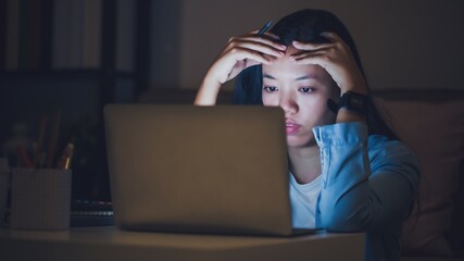 Asian woman student or businesswoman work late at night. Concentrated and feel sleepy at the desk in dark room with laptop or notebook.Concept of people work hard and burnout syndrome. - 411824102