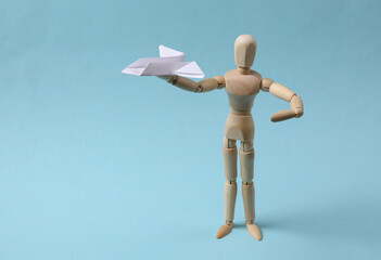 Wooden puppet with paper airplane on blue background