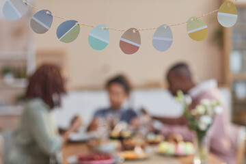 Background image of Easter decorations shaped as Easter eggs with blurred African-American family in background, copy space
