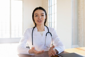 Portrait of young Caucasian female doctor in medical uniform sit at desk in hospital talk on video...