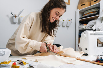 Happy nice girl seamstress cutting fabric while working in atelier