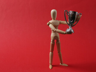 Wooden puppet holding the winner cup on red background