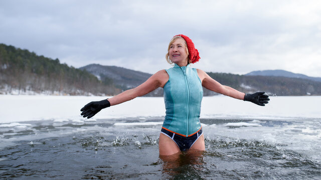 Front view of active senior woman in swimsuit outdoors in water in winter, cold therapy concept.