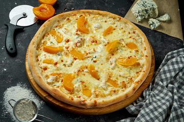 Oven-baked Italian pizza with 4 types of cheese and canned peach in a composition with ingredients on a dark background. Close up view