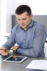 Businessman working with tablet computer in modern office. Headshot of male entrepreneur or company director at workplace. Business concept