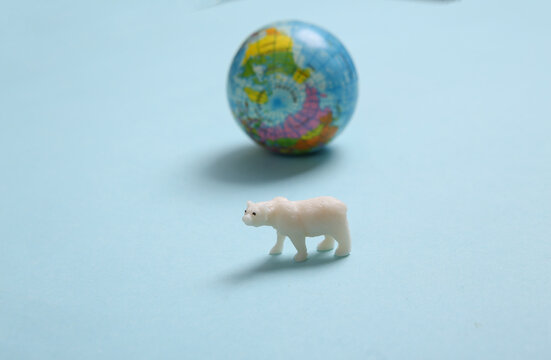 Polar bear figurine and model of the planet earth on a blue background. Save wild animals, global warming concept