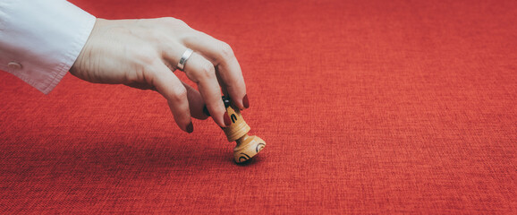 Una mano de mujer come una ficha de ajedrez, la reina blanca, sobre un fondo granate o rojo oscuro.