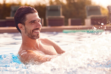 Smiling Man Splashing Water On Summer Vacation In Outdoor Swimming Pool