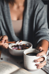 A young girl drinks morning coffee, eats a healthy breakfast and reads a book.