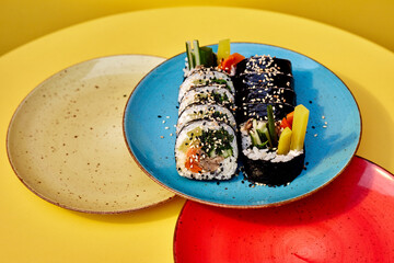 Delicious traditional Japanese food with sushi rolls. On a yellow background. Served on a blue plate with chopsticks. Sushi with rice, sesame, fish and vegetables