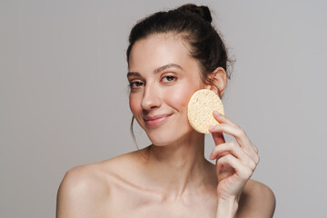 Happy half-naked woman smiling and using cosmetic sponge