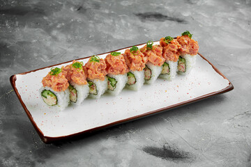 Japanese sushi roll with crab, avocado and spicy tuna in a white plate on a gray background