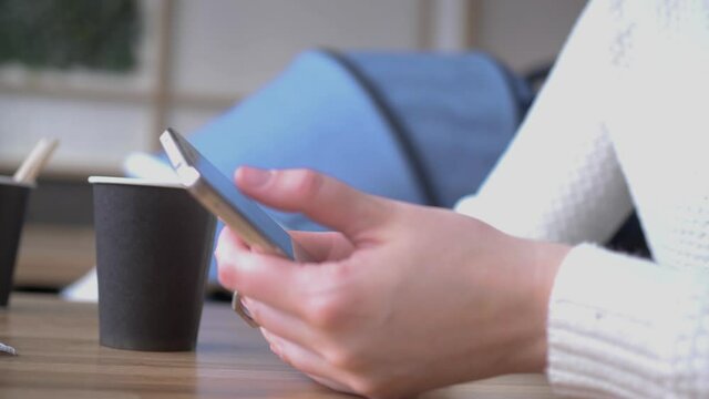 Girl in a cafe uses a tablet and drinks delicious aromatic coffee. Young woman in cafe works with a smartphone. Woman chatting, drinking coffee and relaxing. Close-up.