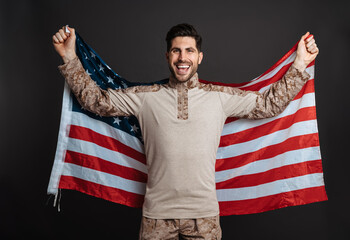Happy masculine military man smiling while posing with american flag
