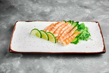 Classic Japanese sashimi set of raw shrimp with lime, cucumber on a white plate on a gray...