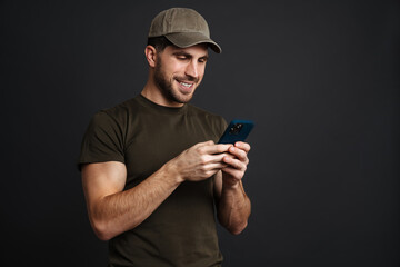 Happy masculine military man smiling and using mobile phone