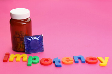 Word IMPOTENCY, jar of pills and condom on pink background