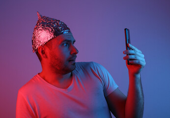 Crazy Bearded Man in a foil hat Holds smartphone in red-blue neon light. 5g. Conspiracy theory