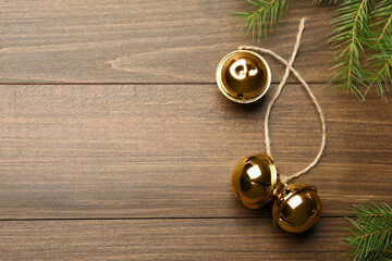 Fototapeta na wymiar Golden sleigh bells with rope and fir branches on wooden background, flat lay. Space for text