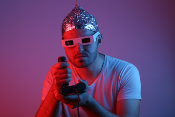 Bearded Man in foil hat and 3d glasses with joystick playing video game in red blue neon light.