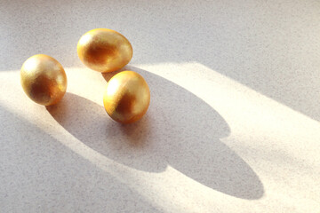 Three painted eggs in golden color on the kitchen table in the sun, top view