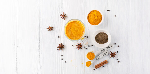 Golden turmeric latte in glass, spices and cinnamon on white wooden background.