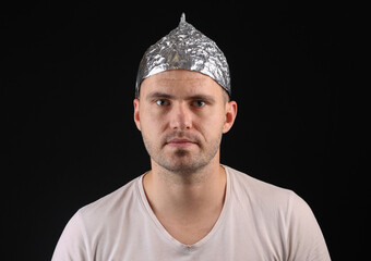 Portrait of a serious man in aluminum foil hat on a black background