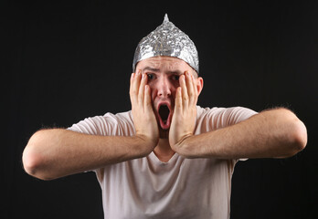Portrait of a scared man in aluminum foil cap on black background