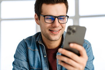 Happy handsome man in eyeglasses smiling and using mobile phone