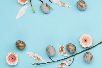 Easter Decoration with gray golden eggs, quail feathers, flowers on blue background. Happy Easter card concept, top view.