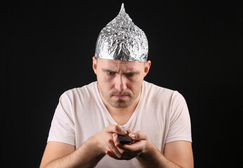 Crazy Man in aluminum foil hat using tv remote on black background