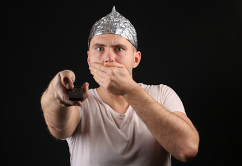 Crazy Man in aluminum foil hat using tv remote on black background