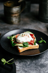 Breakfast. Sandwich with ham, poached egg, avocado and spinach in a plate on a dark background