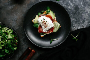 Breakfast. Sandwich with ham, poached egg, avocado and spinach in a plate on a dark background