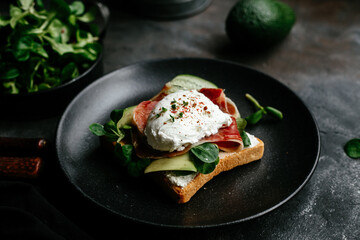 Breakfast. Sandwich with ham, poached egg, avocado and spinach in a plate on a dark background