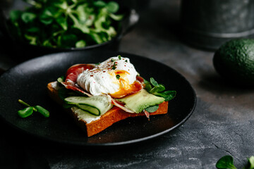 Breakfast. Sandwich with ham, poached egg, avocado and spinach in a plate on a dark background