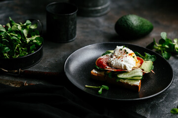 Breakfast. Sandwich with ham, poached egg, avocado and spinach in a plate on a dark background