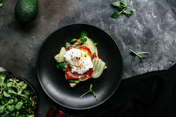 Breakfast. Sandwich with ham, poached egg, avocado and spinach in a plate on a dark background